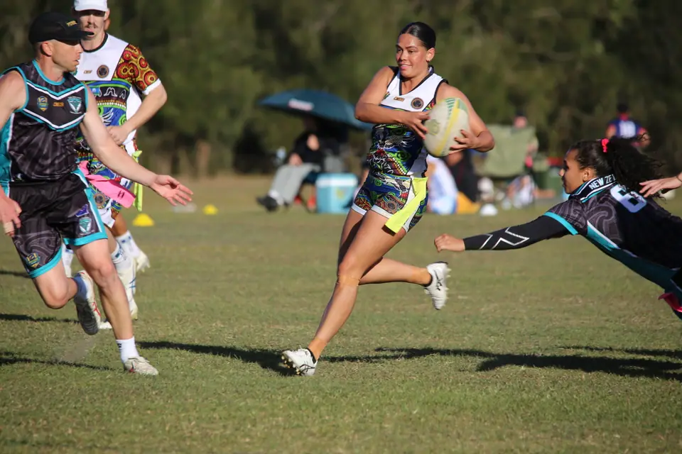 An AIO player carries the ball at pace as a defender dives to take her tag, 2024 Australian Invitational Challenge
